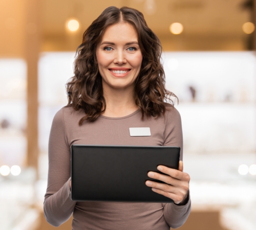 a store assistant smiling, whilst stood in a jewellery store, holding a tablet