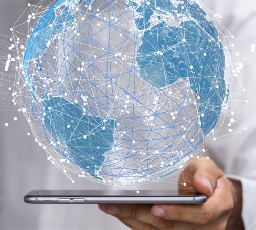 A male in a white shirt is holding out a black mobile phone. Emerging from the phone is a globe, which has a magnitude of lines representing people being connected across the World Wide Web