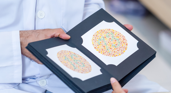 Someone is holding a book with two colour blind tests displayed, to attempt to pick out the number shown.